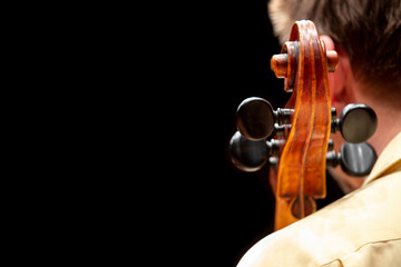 A view from behind of a cello player sitting and having his instrument leaning on his shoulder making only the scroll and pugs visible © Janisphoto