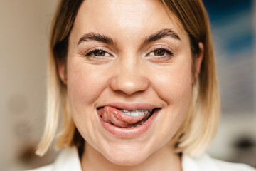 Young woman smiling while licking her brace indoors