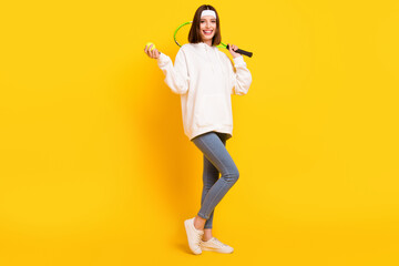 Fototapeta na wymiar Photo of sportive lady hold racket ball wear white headband sweatshirt jeans shoes isolated yellow color background