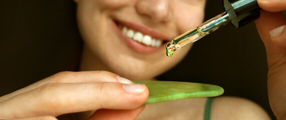 A woman shows a jade gouache face board to the camera. Apply the serum to a jade scraper. Selective focus. © A_sm