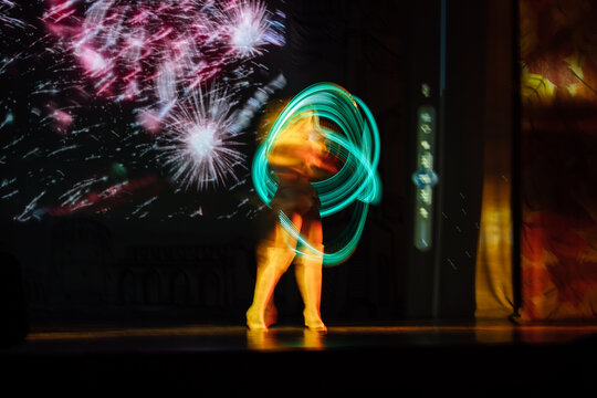 an artist on stage with glowing hoops. a girl in an LED suit performs in a bright show in the dark. the multicolored hula hoop glows. dancing and gymnastics