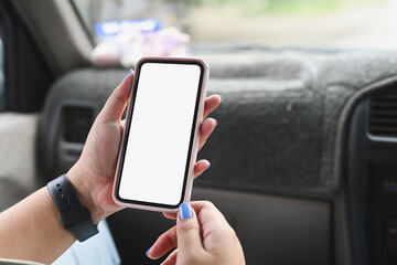 Close up image of a young woman using a white blank screen smartphone while sitting in the passenger seat.