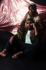 Two Malaysian Indian men in a studio setting with cloth flying in the background, posing against a...