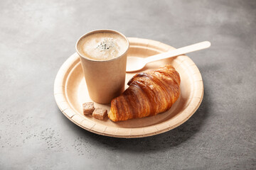 Cup of hot coffee and fresh croissant in disposable craft paper tableware