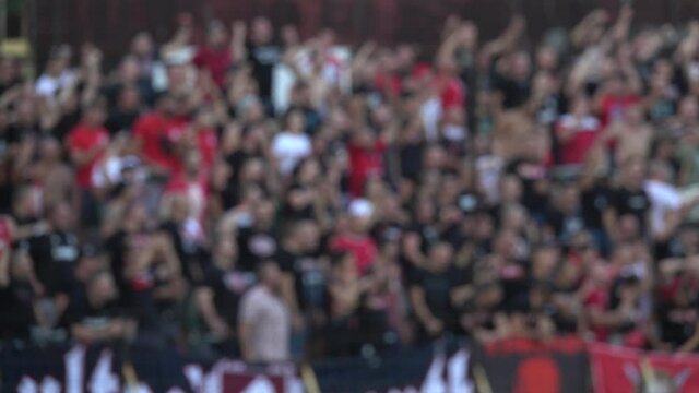 Many fans supporting soccer team at stadium. Blurred crowd of people at football stadium. Slow motion