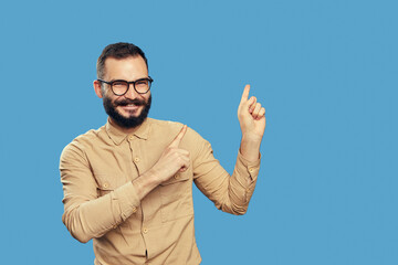 Naklejka premium Excited man points aside on empty space with both forefingers, advertises copy space for your advertising content, wears beige shirt, eyeglasses