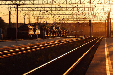 Fototapeta na wymiar railway platform at sunset. a deserted provincial railway station. beautiful golden light of the sun at sunset. travel time by train