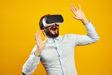 Excited young male wearing virtual reality helmet touching the air, isolated over yellow background. Horizontal studio shot.