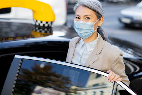 Mature woman wearing protective face mask opening taxi door