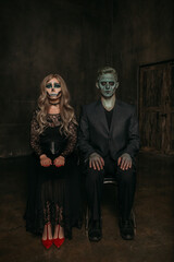 The image of a skeleton girl and the image of a Frankenstein man on Halloween in the dark. an image for a couple on Halloween. a woman and a man are sitting on chairs, hands on their knees