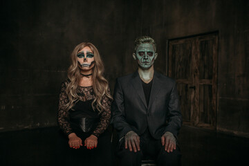 The image of a skeleton girl and the image of a Frankenstein man on Halloween in the dark. an image for a couple on Halloween. Sitting on chairs, hands on knees, looking at the camera