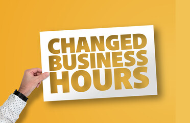hand holding CHANGED BUSINESS HOURS sign against orange background