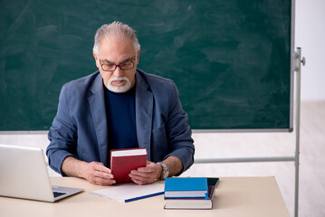 Old male teacher holding book in the classroom