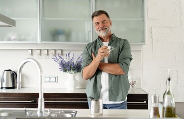Happy mature man drinking coffee at home in the kitchen, enjoying hot drink in the morning on...