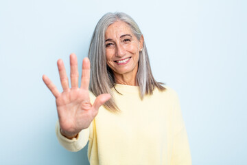 middle age gray hair woman smiling and looking friendly, showing number five or fifth with hand...
