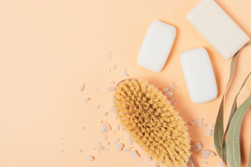Massage brush with soap bars and bath salt on peach background