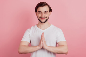 Portrait of charming pleading guy hold palms together look camera on pink background