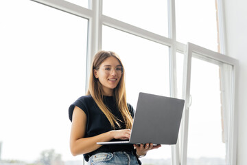 young pretty woman sitting near the window with a laptop at home on the windowsill