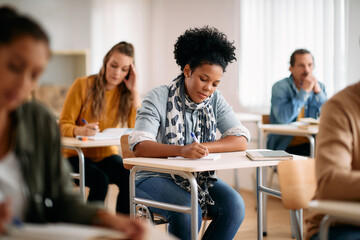 African American female student writes while learning during class at university classroom.