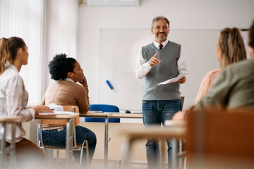 Happy mature professor gives lecture to adult students in classroom.