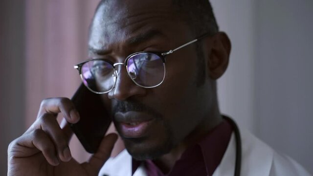 Doctor man talk on phone call, black physician work in hospital health care Spbas. Handsome confident male in glasses talk to patient, have smartphone conversation. Concept closeup
