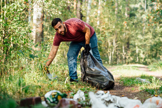 Mid Adult Male Environmentalist Collecting Garbage In Forest