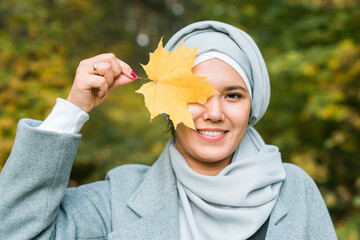 Autumn muslim woman holding maple leaf outdoors in sunny day. Beautiful arab wearing hijab girl in...