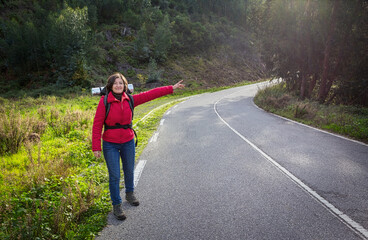 A woman tourist, in a jacket, hitchhiking on the road, walks along the Portuguese forest roads. Stops fellow travelers.