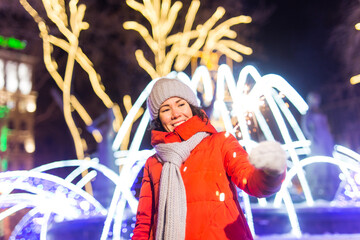 Girl holding a sparkler in her hand. Outdoor winter city background, snow, snowflakes.