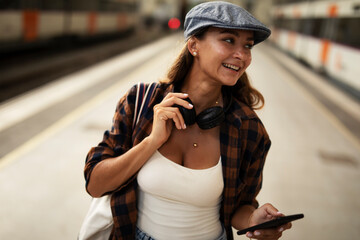 Young woman waiting for the train standing at the railway station. Beautiful girl using the phone while waiting for the train.