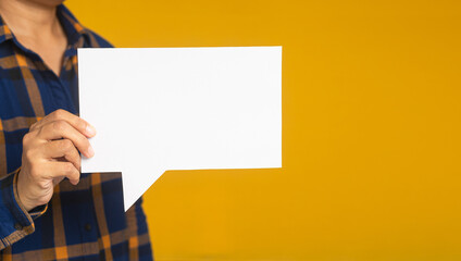 Business and speech bubble concept. Businessman in a blue shirt holding an empty speech bubble paper while standing on a yellow background in the studio. Space for text. Close-up photo