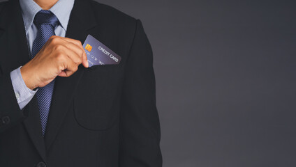 Businessman in a suit holding a mockup blue credit card in a suit pocket while standing with gray background in the studio. Space for text. Business and finance concept