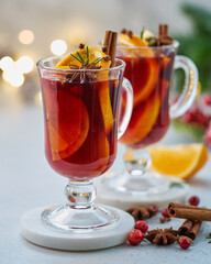 Two glasses of red mulled wine. Hot winter beverage with cinnamon, cardamom and clove, orange and anise, cranberry, fir needles. Selective focus, blurred background, bokeh, vertical, closeup