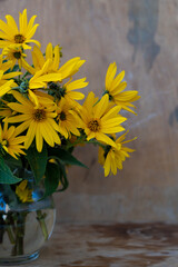 A bouquet of yellow Jerusalem artichoke flowers in a glass vase on a wooden background. Postcard with place for text. A simple wild flower that looks like a chamomile. Copy space.