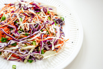 Coleslaw cabbage salad with cabbage, carrots, herbs and sesame seeds on a white plate. Healthy eating, vegan food.