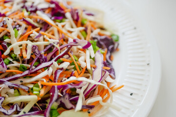 Coleslaw cabbage salad with cabbage, carrots, herbs and sesame seeds on a white plate. Healthy eating, vegan food.