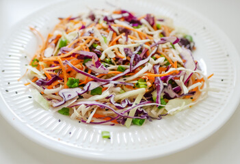 Coleslaw cabbage salad with cabbage, carrots, herbs and sesame seeds on a white plate. Healthy eating, vegan food.