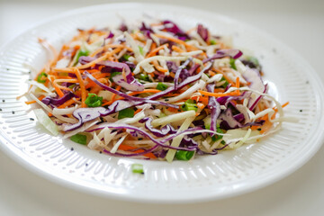 Coleslaw cabbage salad with cabbage, carrots, herbs and sesame seeds on a white plate. Healthy eating, vegan food.