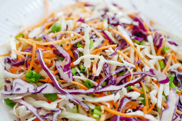 Coleslaw cabbage salad with cabbage, carrots, herbs and sesame seeds on a white plate. Healthy eating, vegan food.