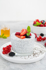 Vanilla chia pudding with fresh berries and honey in a glass on a gray concrete background. Superfoods concept. Copy space.