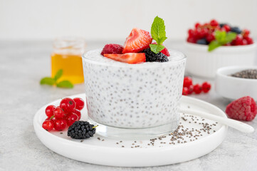 Vanilla chia pudding with fresh berries and honey in a glass on a gray concrete background. Superfoods concept. Copy space.