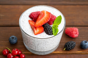 Vanilla chia pudding with fresh berries and honey in a glass on a dark wooden background. Superfoods concept. Copy space.