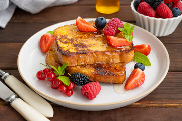 A stack of French toast on a plate with fresh berries, almond petals and honey on a dark wooden background. Delicious breakfast. Copy space.