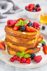 A stack of French toast on a plate with fresh berries, almond petals and honey on a gray concrete background. Delicious breakfast. Copy space.