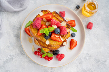 A stack of French toast on a plate with fresh berries, almond petals and honey on a gray concrete background. Delicious breakfast. Copy space.