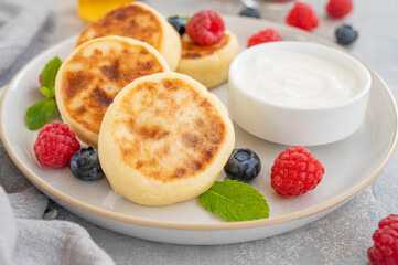 Cottage cheese pancakes with fresh berries, sour cream and honey on a gray concrete background. Homemade traditional Ukrainian and Russian syrniki.