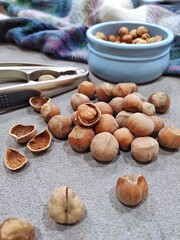 close-up image of selective focus of hazelnuts in shells and a plate with peeled hazelnuts, against a dark background. Some are shot and some are cracked. Cracking nuts requires a metal nut cracker.