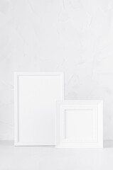 Two white wood blank rectangle and square photo frames on soft light table, plaster wall in modern minimal simple style, copy space, vertical. Mockup for design, showing, presentation, portfolio.