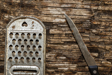 An old rusty kitchen grater and kitchen knife against a rotting