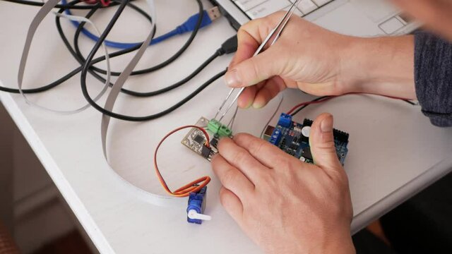 A male programmer creates robotics, an arduino board controls servo motors. DIY mechanics, programming through codes on a laptop. Technologies of the future. close up